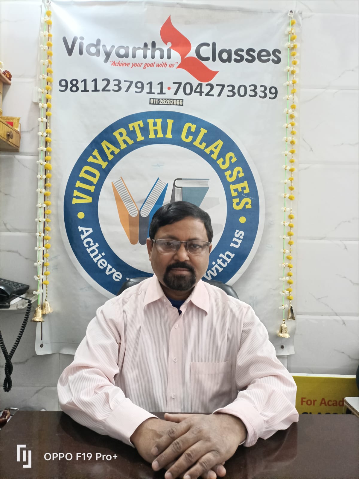 SK Vidyarthi, founder and director of Vidyarthi Classes, smiling in a formal suit, seated in an office environment